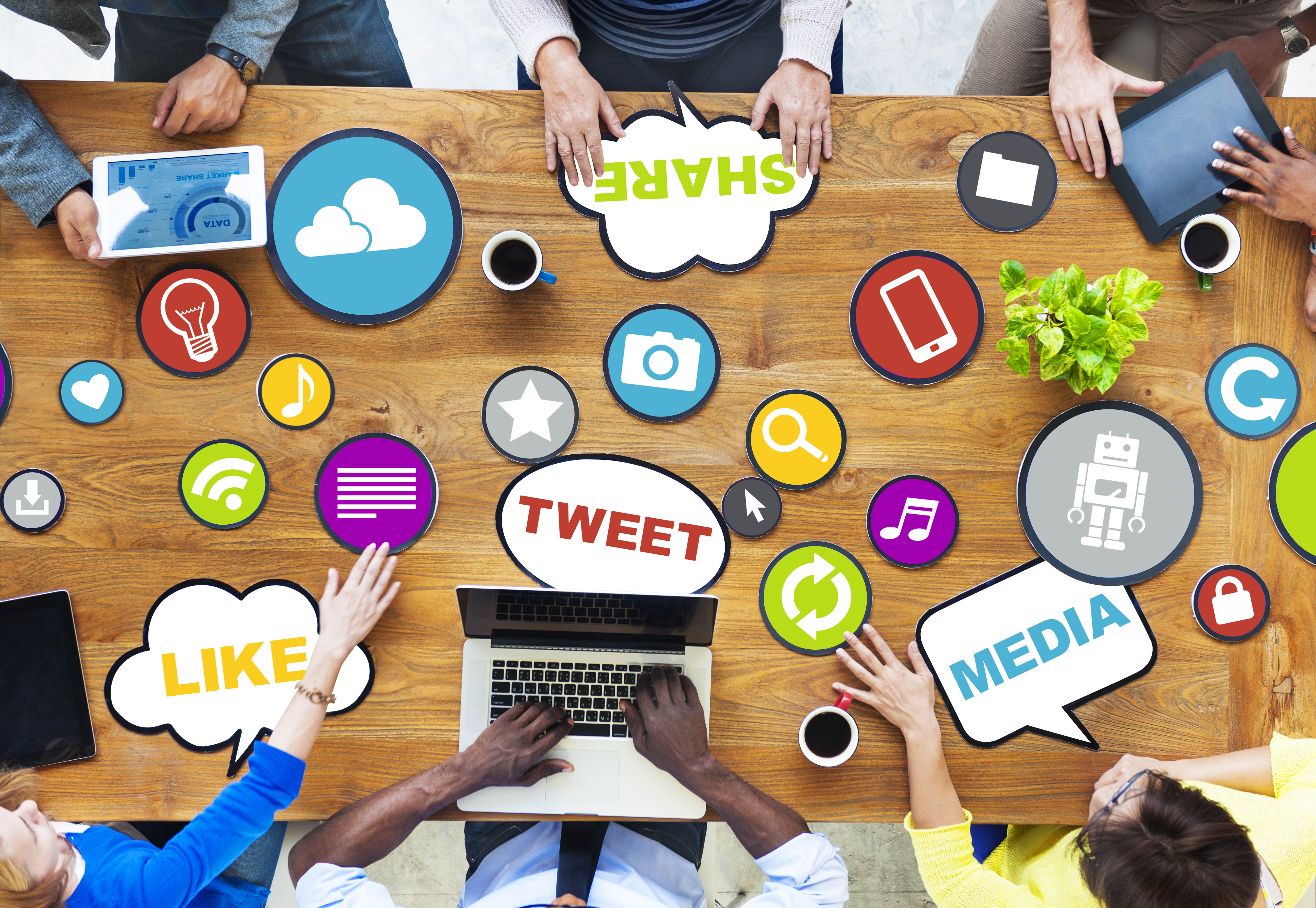 Six people sit at a long table, speaking to each other about their ideas on how to use social media. The word 'Like' is in the bottom left, the word 'Tweet' is in the bottom center, the word 'Media' is in the bottom right, and the word 'Share is in the top center.' 